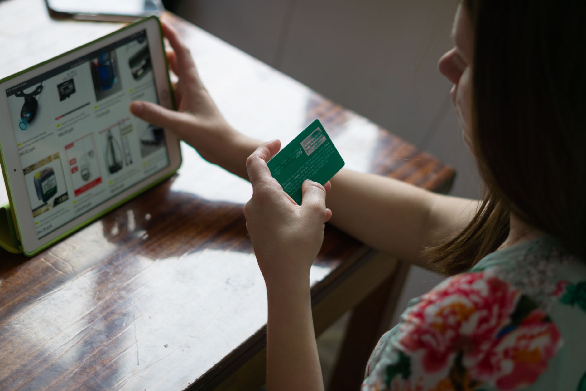 A woman uses a credit card for online shopping on a tablet at a wooden table.