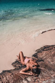 Woman in a swimsuit relaxing on a serene tropical beach during summer.