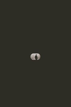 A silhouette of a man seen through a tunnel opening within a dark setting, creating a mysterious mood.