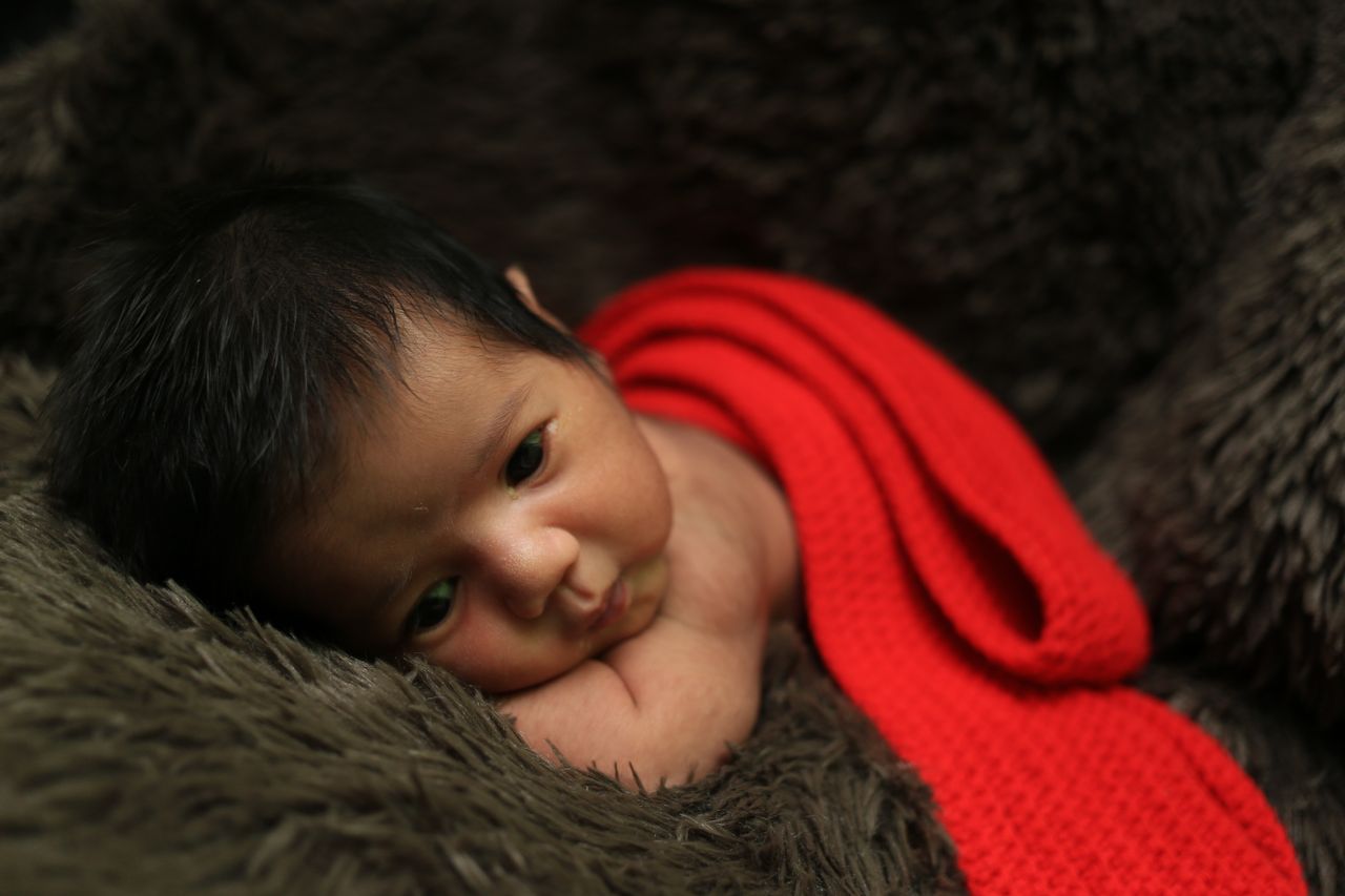 cozy newborn baby lying on brown fabric wrapped in a red crochet blank