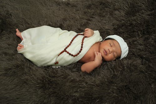 Free Infant Sleeping in White Cloth and Cap Holding Prayer Beads Stock Photo