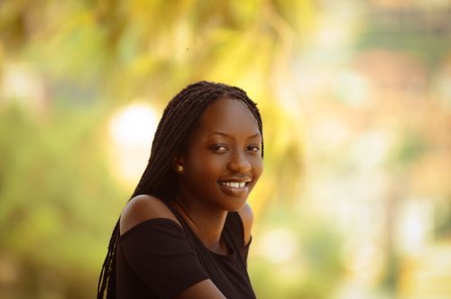 Free Portrait of a cheerful young woman with braided hair wearing a black top, captured in an outdoor setting with a blurred background. Stock Photo