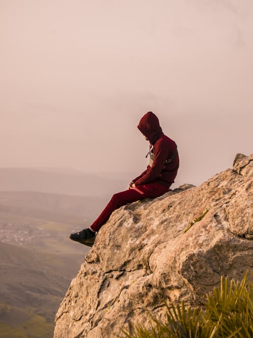 A Person in Red Hoodie Sitting on the Rock