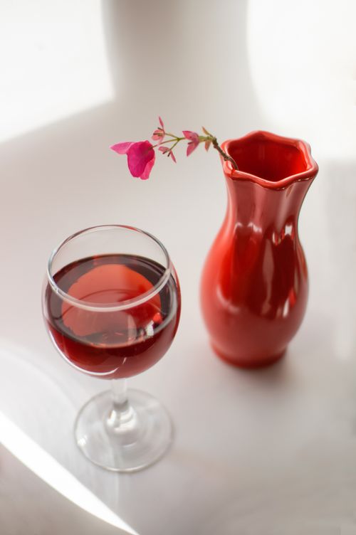 Free Sophisticated still life of red wine in a glass beside a matching vase with flower. Stock Photo