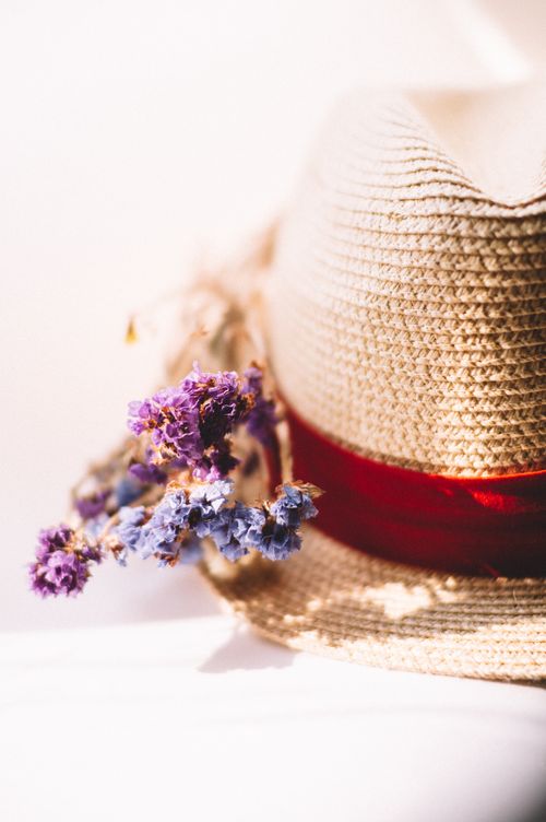 Free Close-up of a stylish fedora hat adorned with vibrant purple flowers on a bright surface. Stock Photo