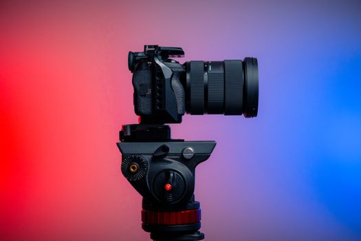 Side profile of a DSLR camera mounted on a tripod, highlighted by dramatic red and blue lighting.