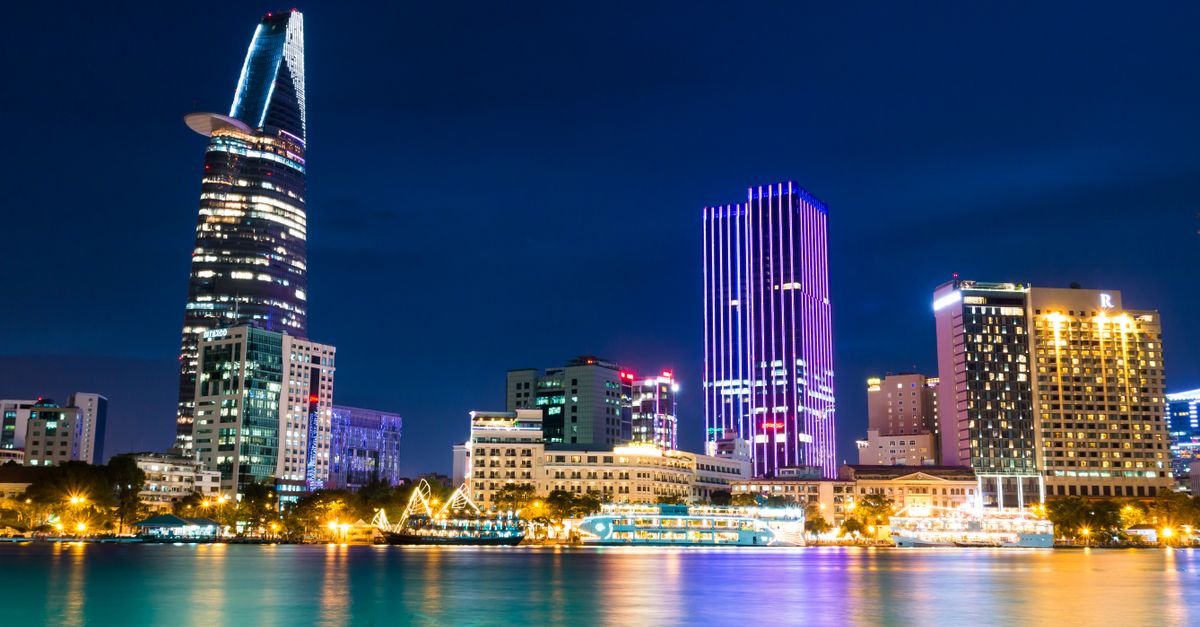 Vibrant night view of Ho Chi Minh City skyline with illuminated skyscrapers reflecting in the river.