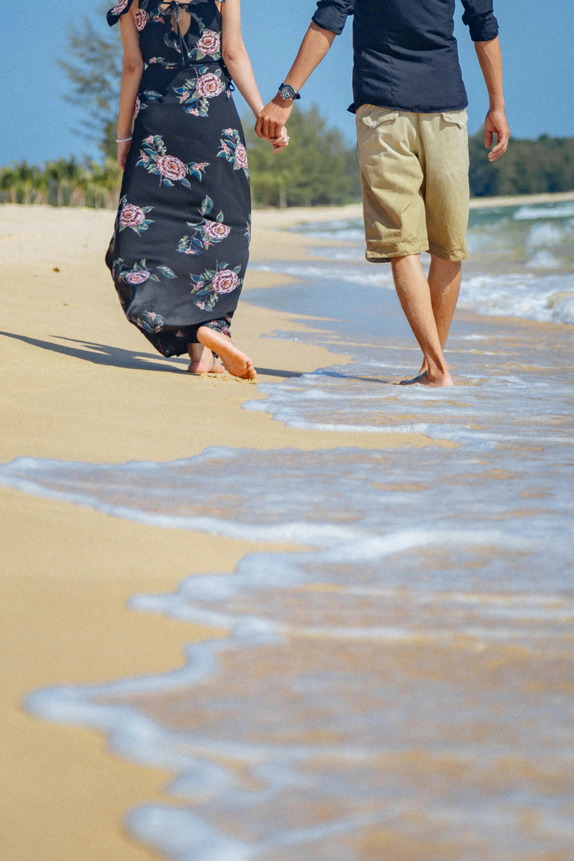 crop unrecognizable couple holding hands while strolling on sea beach