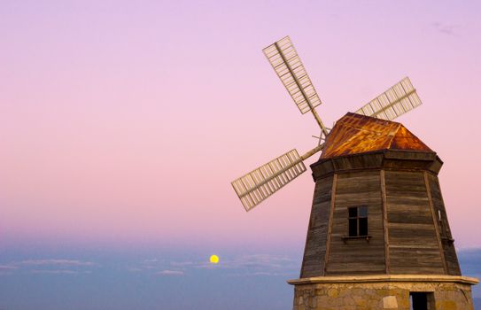 Wooden windmill silhouetted against a beautiful pink sunset sky, creating a dramatic and serene scene.