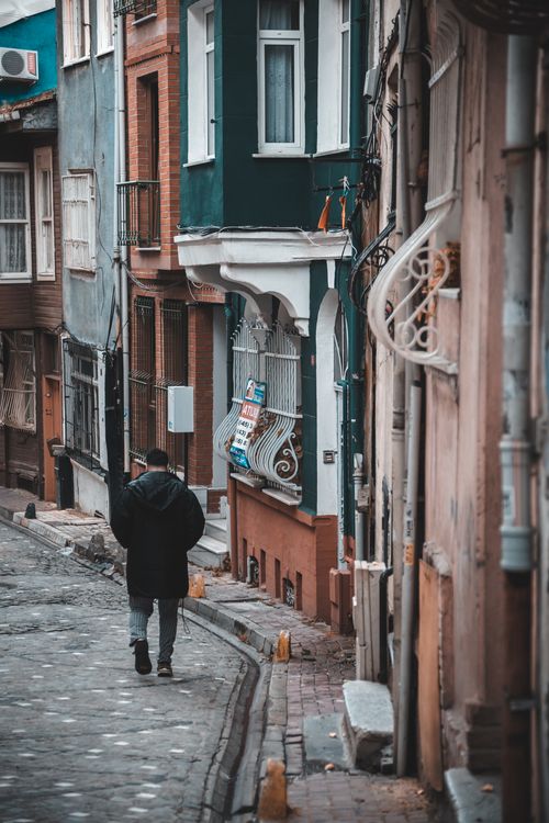 Free A man strolls through a picturesque cobblestone street lined with vintage townhouses. Stock Photo