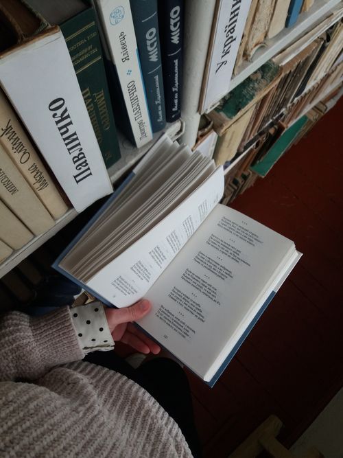 Free A person holding an open book in front of a bookshelf filled with books in a library. Stock Photo