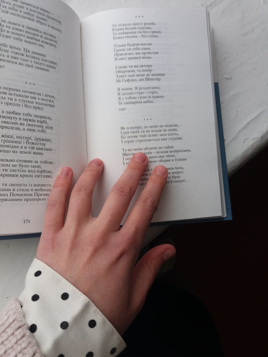 Hand placed on an open book displaying printed text on a table.