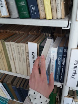 Close-up of a person choosing a book from a library bookshelf, enhancing knowledge.