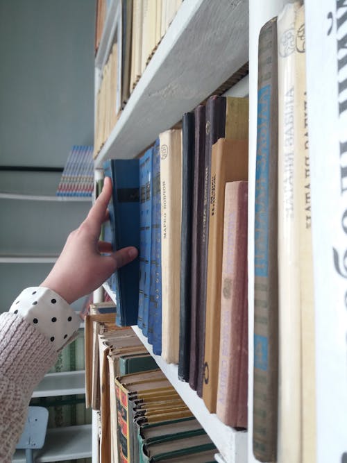 A Hand Holding a Book in a Bookshelf 