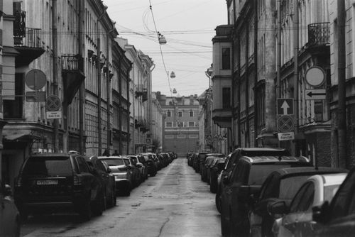 Free Black and white photo of a narrow city street with parked cars and historic buildings. Stock Photo