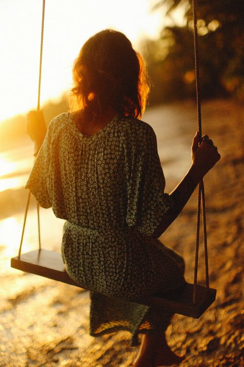 Free A woman in a floral dress swings by the beach during a golden sunset. Stock Photo