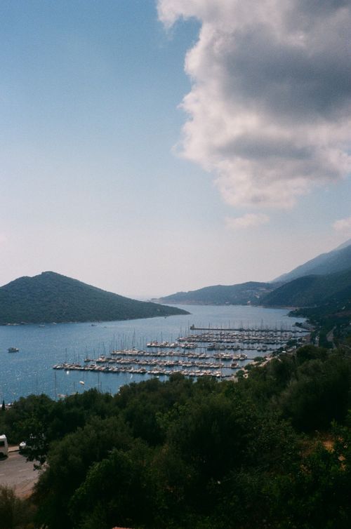 Free Beautiful seaport with sailboats, surrounded by lush mountains under a cloudy sky. Stock Photo