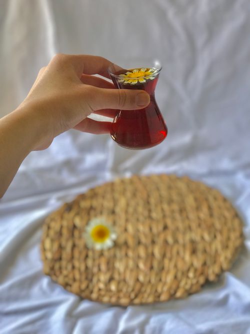 Free A hand holding Turkish tea in a tulip glass with a daisy on a placemat. Stock Photo