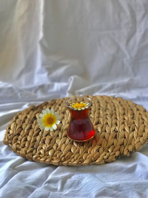 Free A close-up of Turkish tea served in a traditional glass with a chamomile flower on a woven mat. Stock Photo
