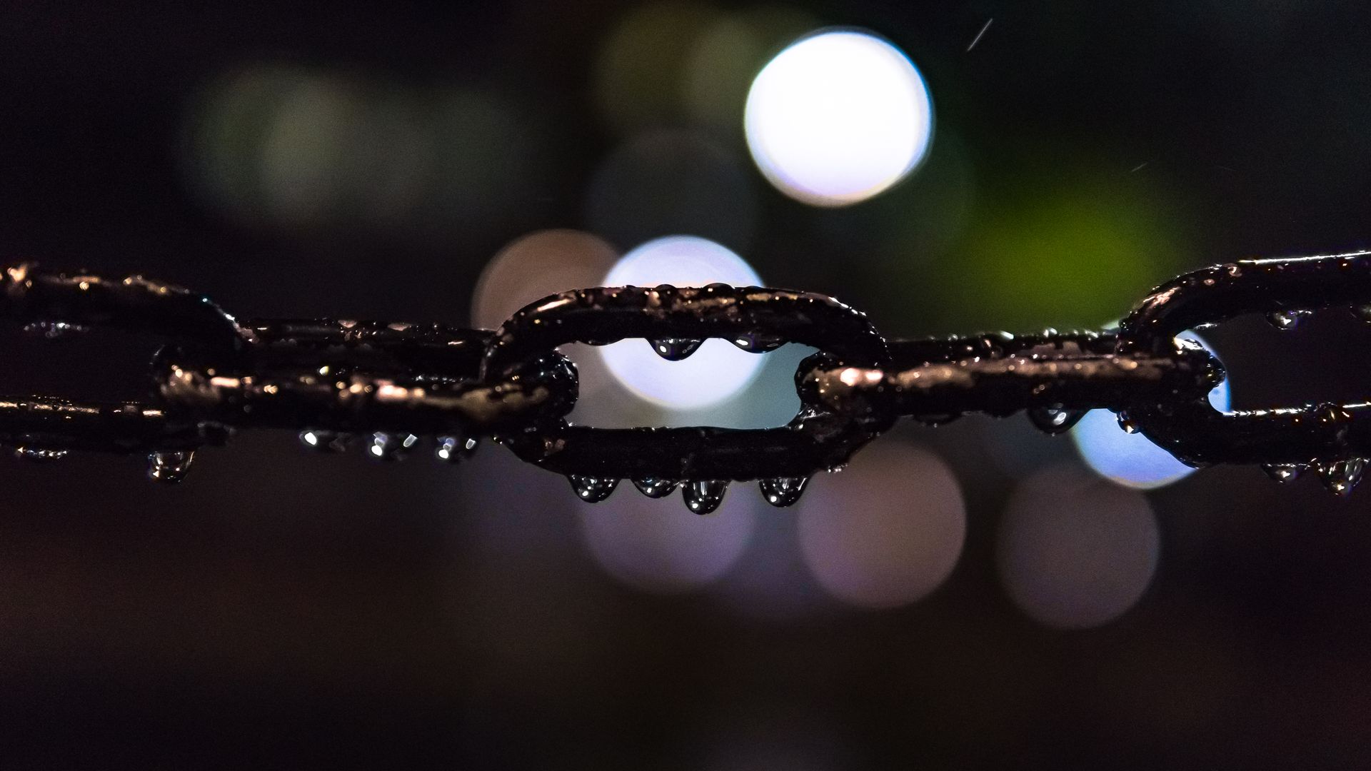 Artistic shot of a wet steel chain with bokeh lights in the background, captured at night.