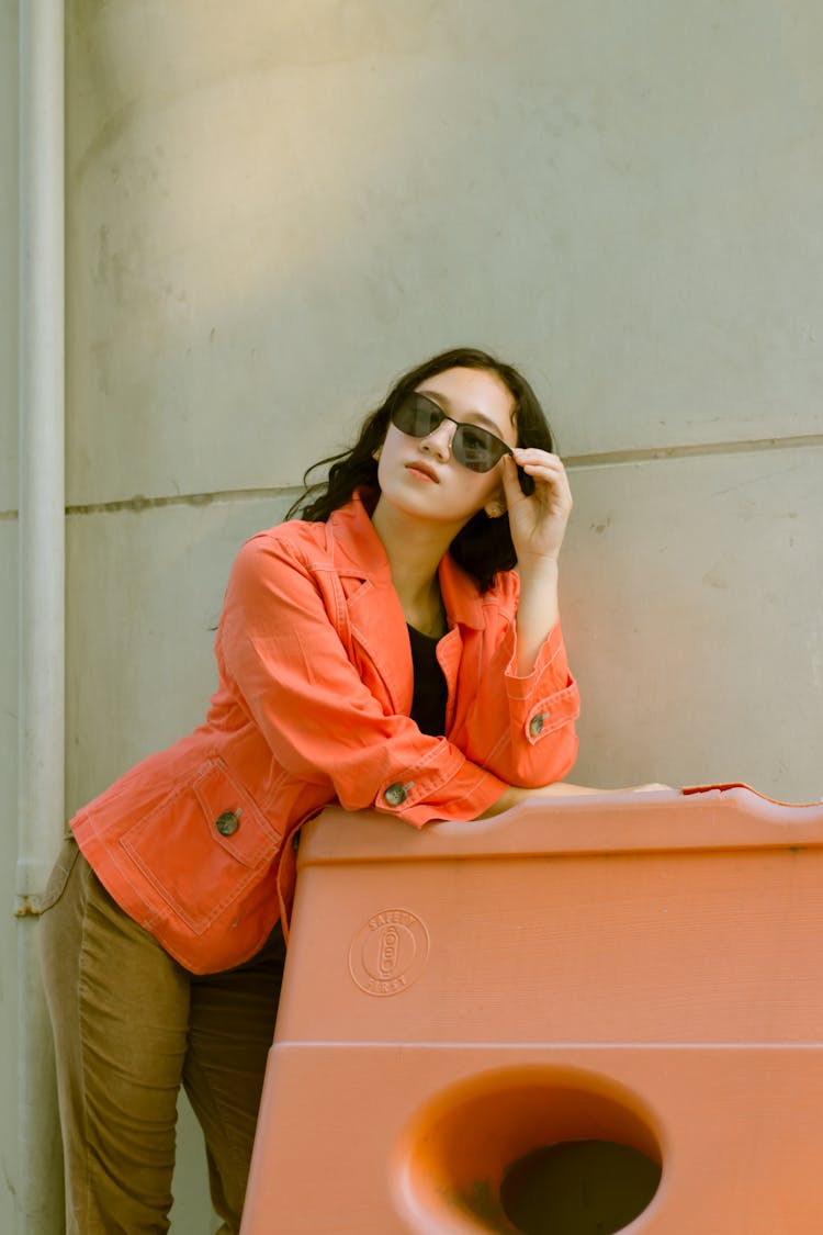 A Woman In An Orange Top Leaning On A Plastic Barricade