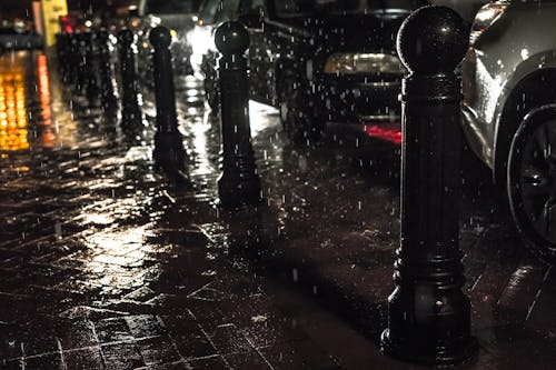 Черные столбики на черном тротуаре под проливным дождем