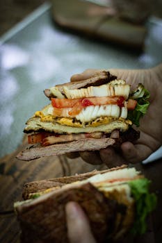 Close-up of a hand holding a stacked gourmet sandwich with fresh ingredients.