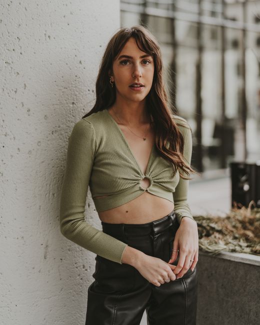 Young adult woman wearing a crop top and leather pants, posing confidently against a textured wall.