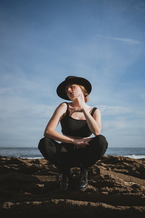 Woman in a Black Hat Crouching on the Beach 