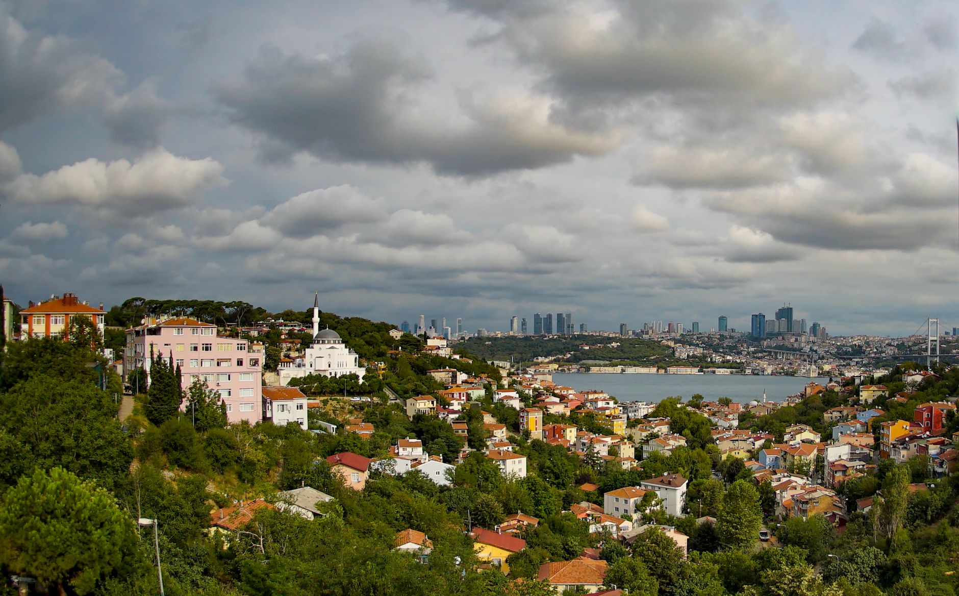 Aerial view of Istanbul's colorful buildings, lush greenery, and Bosphorus with a cloudy sky.