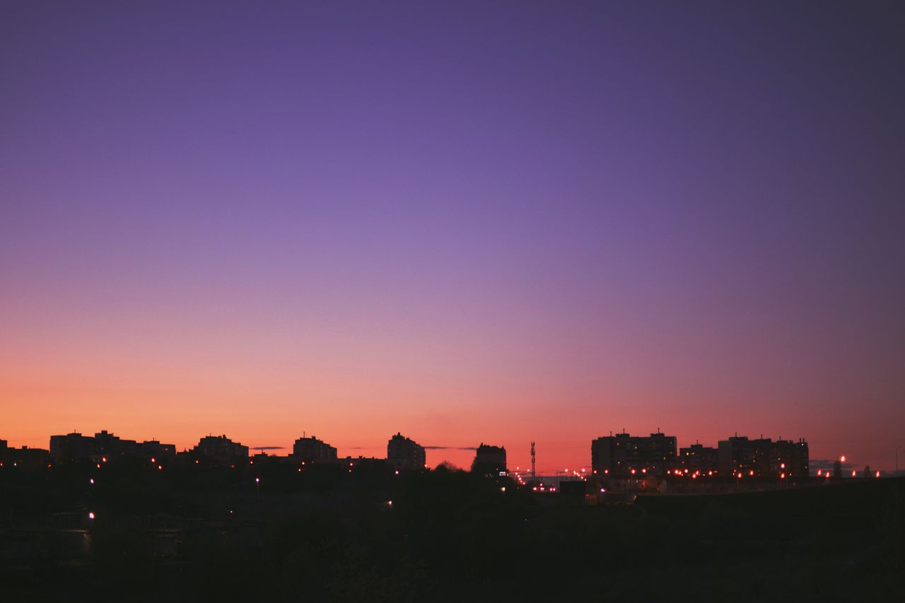 silhouette of city buildings against a vibrant purple and orange sunse