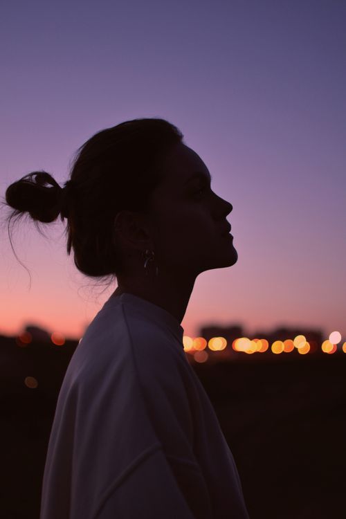 Free Artistic silhouette of a woman against a twilight sky with city lights in the background. Stock Photo