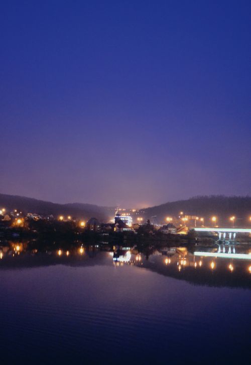 Free A peaceful city skyline at night reflecting on calm waters under a deep blue sky. Stock Photo