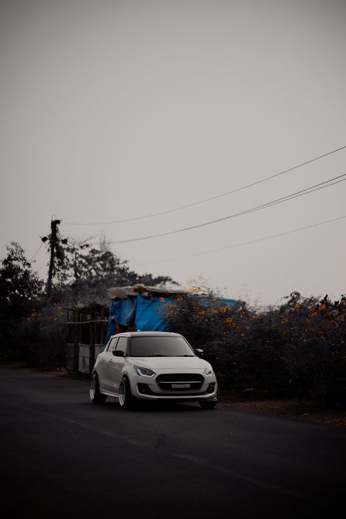 Free A customized white car parked on a quiet rural road with flowers lining the roadside. Stock Photo