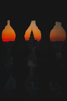 Silhouette of Moscow skyline during a dramatic sunset, viewed through ornate railing.