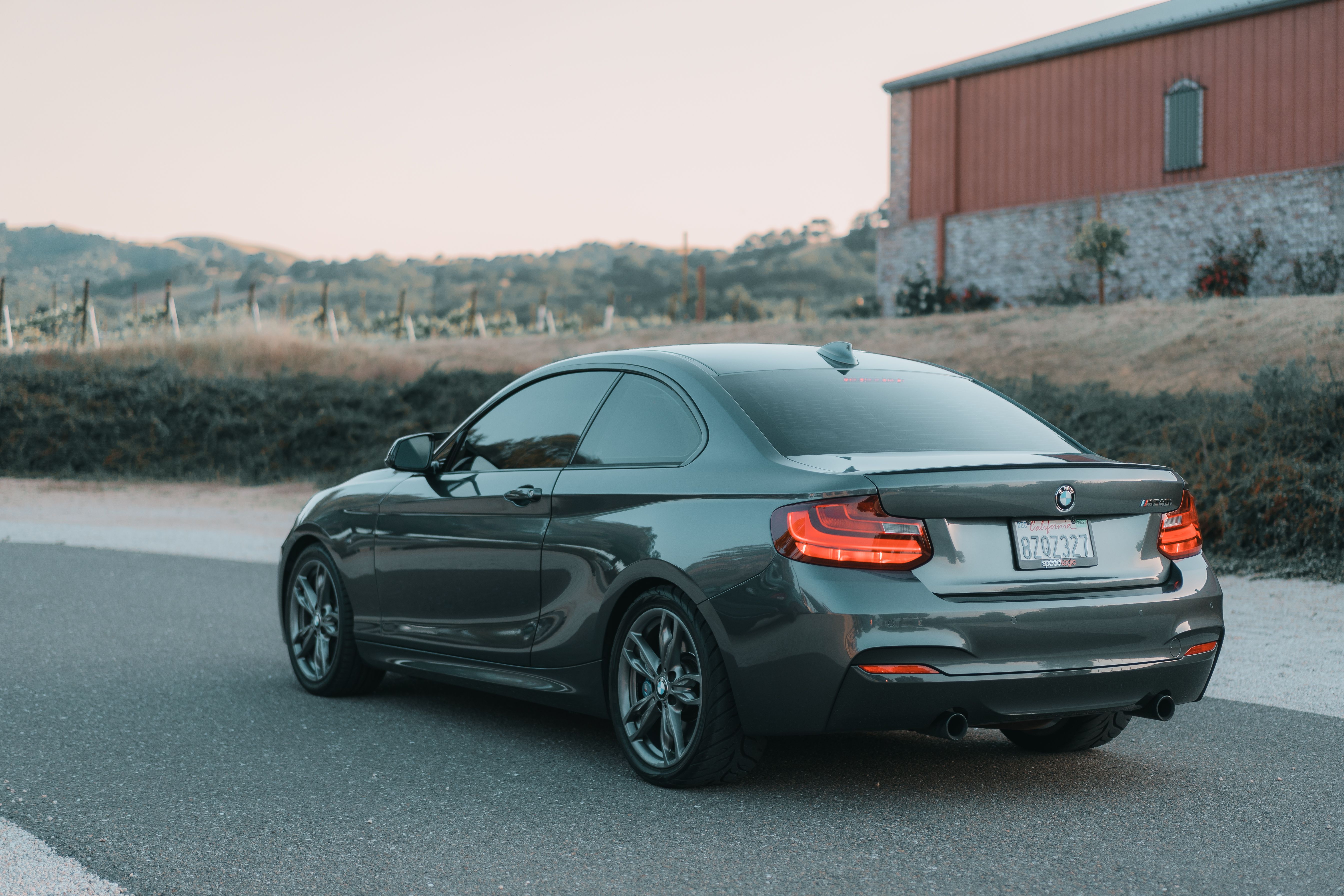 A stylish black BMW parked on a picturesque country road with a rustic barn and vineyard in the background.