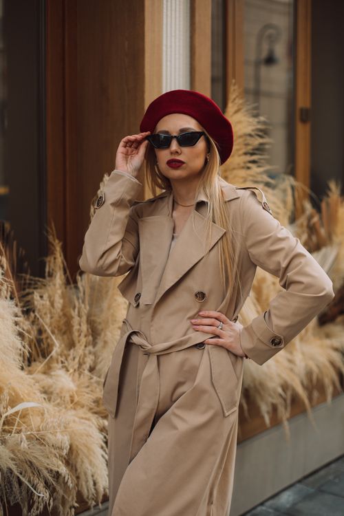 Free Stylish woman in a trench coat and beret adjusting sunglasses outdoors. Stock Photo
