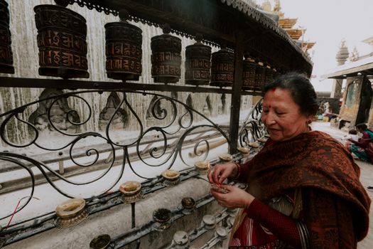 Elderly woman spinning prayer wheels at a temple, highlighting cultural traditions.