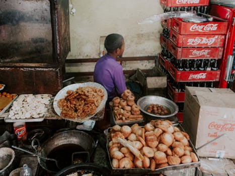 A young street vendor sells traditional snacks in a bustling outdoor market setting.