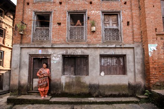 An Indian woman stands by a historic brick facade, capturing traditional architectural details.