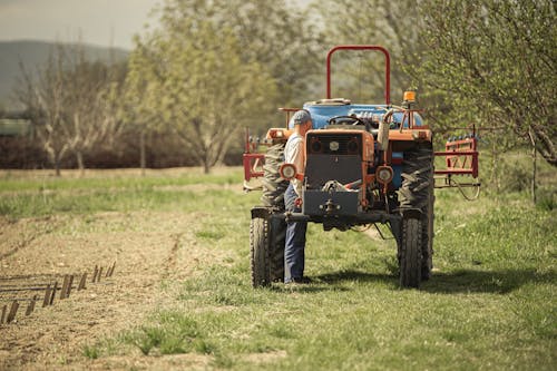 Man Standing Beside a Tractor on Green Grass Field