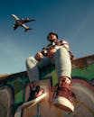 Man Sitting on Wall Covered in Graffiti with Airplane Flying Over His Head