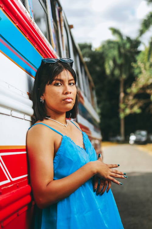 Woman in Blue Spaghetti Strap Dress Leaning on Bus