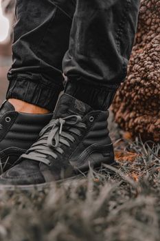 Stylish black sneakers close-up on grass with a textured background, showcasing footwear fashion.