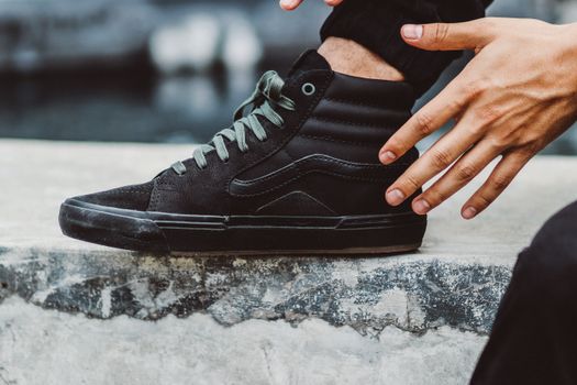 Stylish black high-top sneakers with hands adjusting them on a concrete surface.