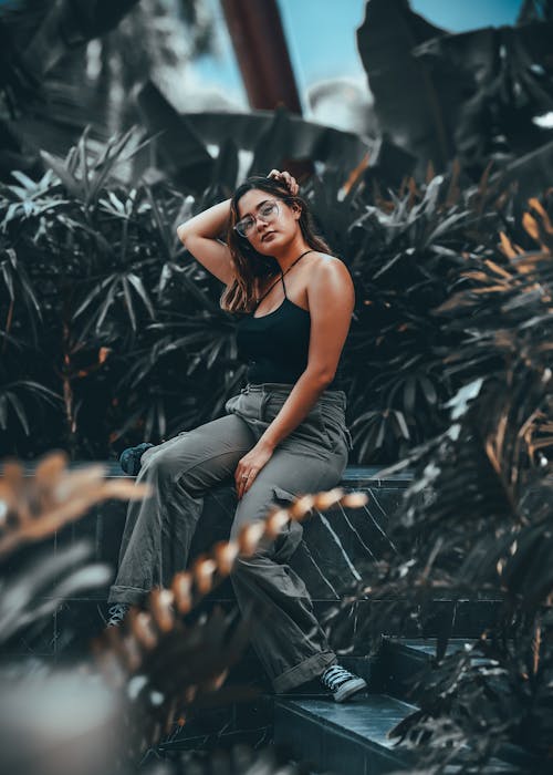 Woman in Black Tank Top Sitting on Concrete Bench Near Green Plants