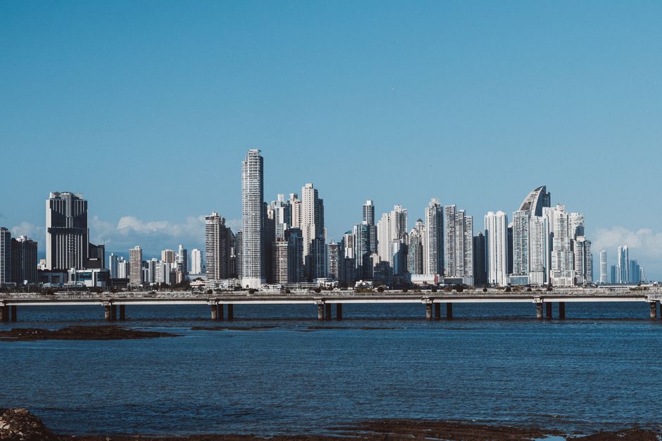 Panama City skyline with towering skyscrapers reflecting in the ocean under a clear blue sky.