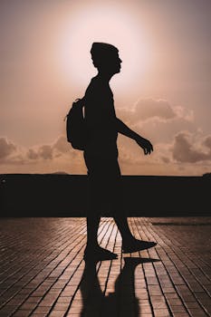 Silhouette of a man walking on a cobblestone street during a beautiful sunset, creating a dramatic backlit scene.