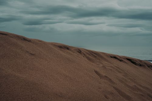 Free Tranquil view of sand dunes meeting the ocean under a cloudy sky, capturing natural calm. Stock Photo
