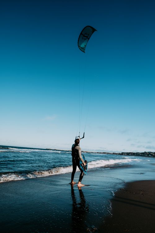 Free Kitesurfer getting ready on a sandy beach with clear blue skies. Stock Photo
